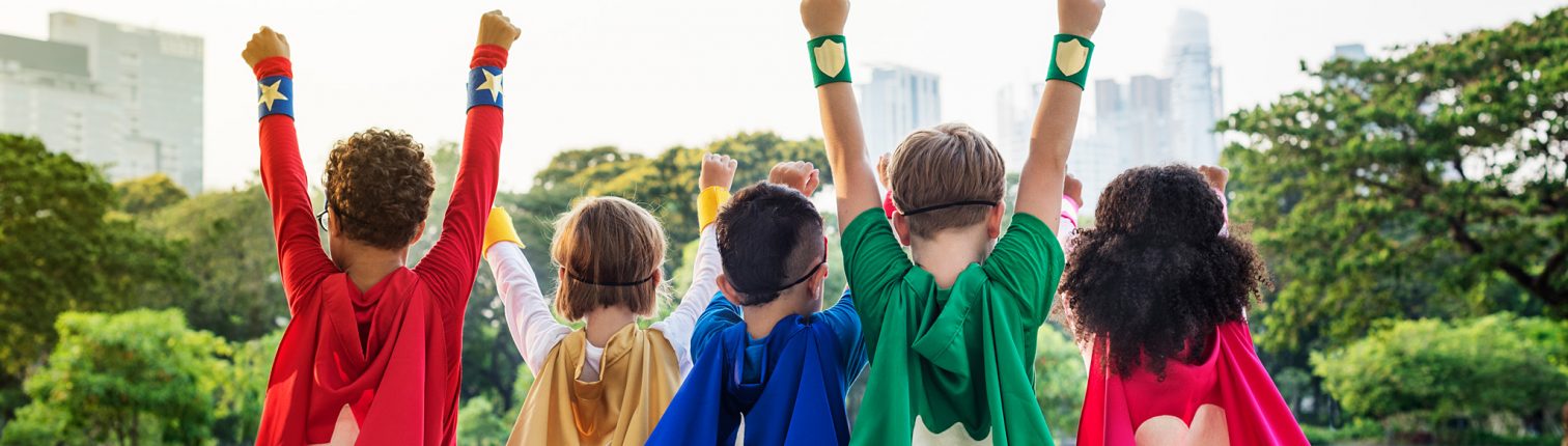 Five children in superhero capes raise their arms in triumph outside facing a city skyline.